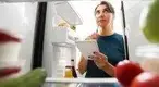 Girl-With-Notebook-Thinking-About-Food-In-Fridge-.webp