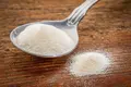 Spoonful of collagen protein powder sitting on a wooden table.