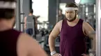 overweight man looking into the mirror in the gym trying to fix his bad habits