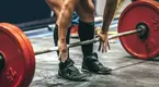 Powerlifter with chaulky hands grabbing a barbell against his shin ready to deadlift.