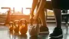 Fit female squating to lift a row of different size kettlebells for her kettlebell training exercises