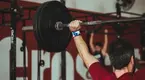 Man performing a full body workout with the barbell overhead carry exercise and overhead press accessory exercises