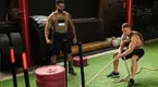 Training partner wearing a weighted vest as his partner does the sled drag exercise