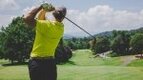 Golfer wearing a titleist hat swinging a hybrid golf club from the tee box with perfect from to avoid golfing injuries.