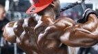 Black bodybuilder doing deltoid shoulder exercise with cable rope machine