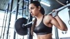 Young fit female with a feminine physique lifting heavy weights on a barbell and avoiding building a manly physique