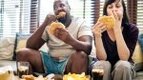 Overweight interracial couple eating unhealthy ultra-processed foods and junk food that causes inflammation