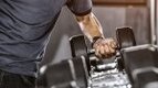 Man lifting a heavy single dumbbell off the dumbbell rack