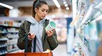 Young female reading the nutritional value of a yogurt label while shopping at the grocery store