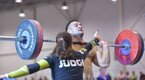 Male crossfit competitor performing a snatch exercise as a judge inspects his form