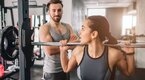 Pretty young female lifting weights at the gym being harassed by a male gym goer