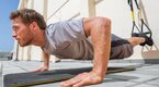 Physically fit man performing the TRX Atomic Pushup outdoors