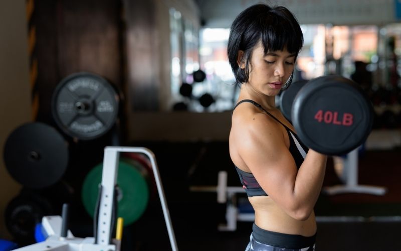 Woman in black sports bra and leggings doing bicep curls with 40 pound dumbbells and intensely looking at her bicep.