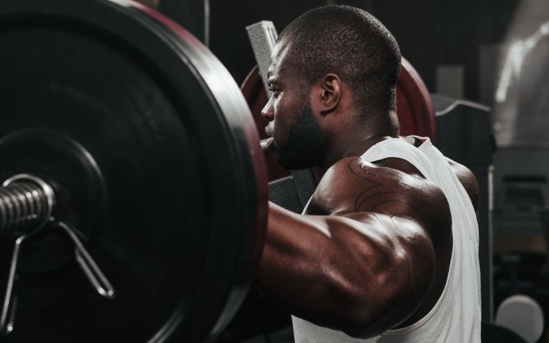 Man wearing white tank standing behind barbell.