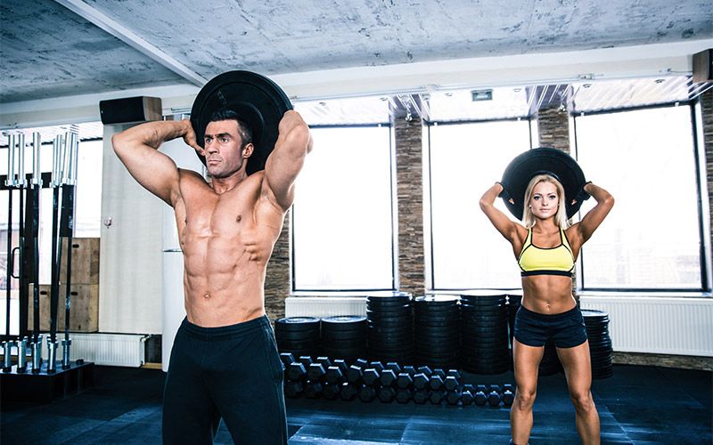 Man and woman performing overhead plate tricep extensions