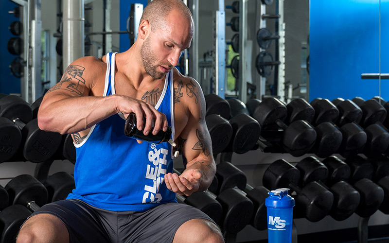 Athletic man sitting on a bench taking vitamins at the gym